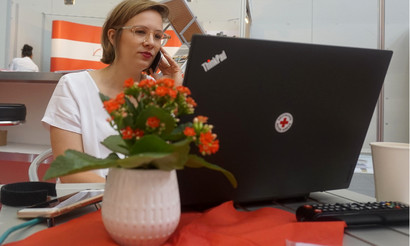 Eine Frau sitzt vor einem Laptop mit einem Logo vom Deutschen Roten Kreuz darauf und telefoniert.