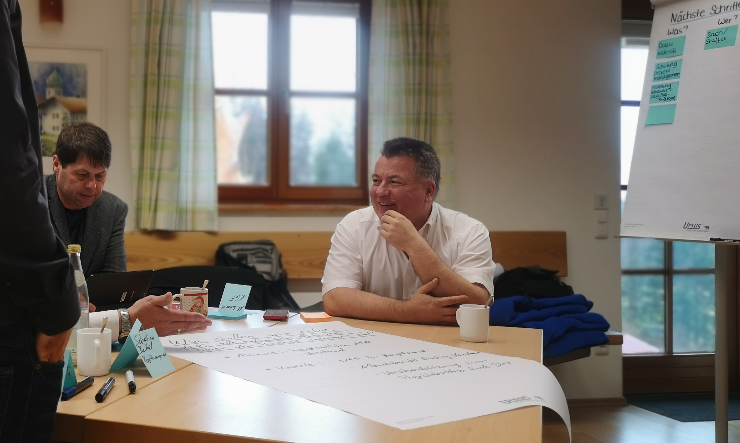 Ein Mitarbeitender des Kreisverband Rosenheim sitzt an einem Tisch vor einem Flipchart und lacht.