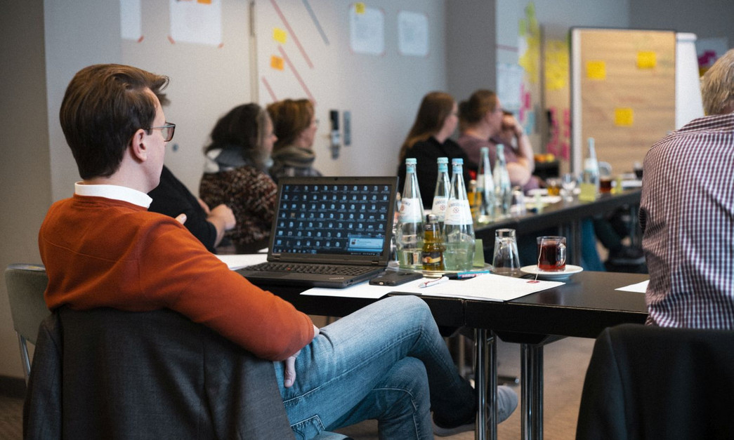 DRK-Nov_2019 Foto aus einem Seminarraum. Ein Mann sitzt in einer Runde vor seinem Laptop.