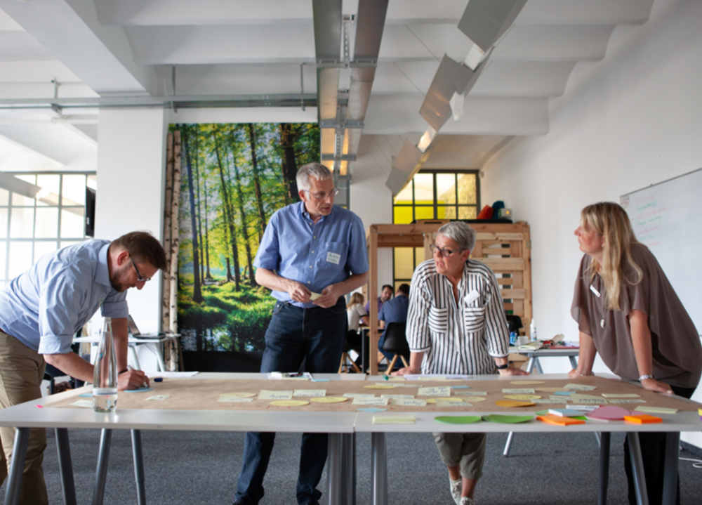Vier Personen stehen an einem großen Malertisch und beraten gemeinsam, wie die Digitalisierung im DRK gestaltet werden kann. 