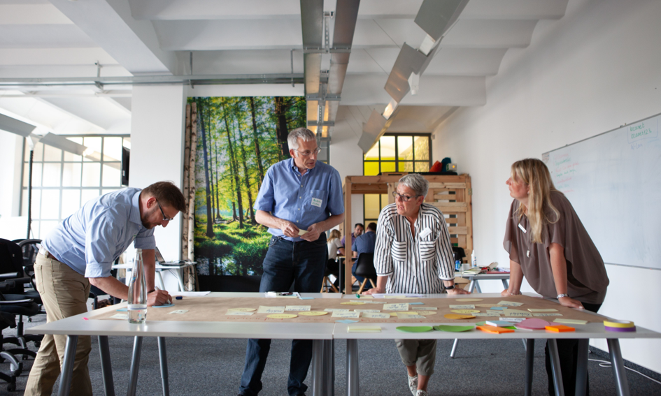 Die Kompetenzzentren Digitalisierung stellen sich für den Newsletter Digitalisierung vor. Vier Personen stehen an einem großen Malertisch und beraten gemeinsam, wie die Digitalisierung im DRK gestaltet werden kann.