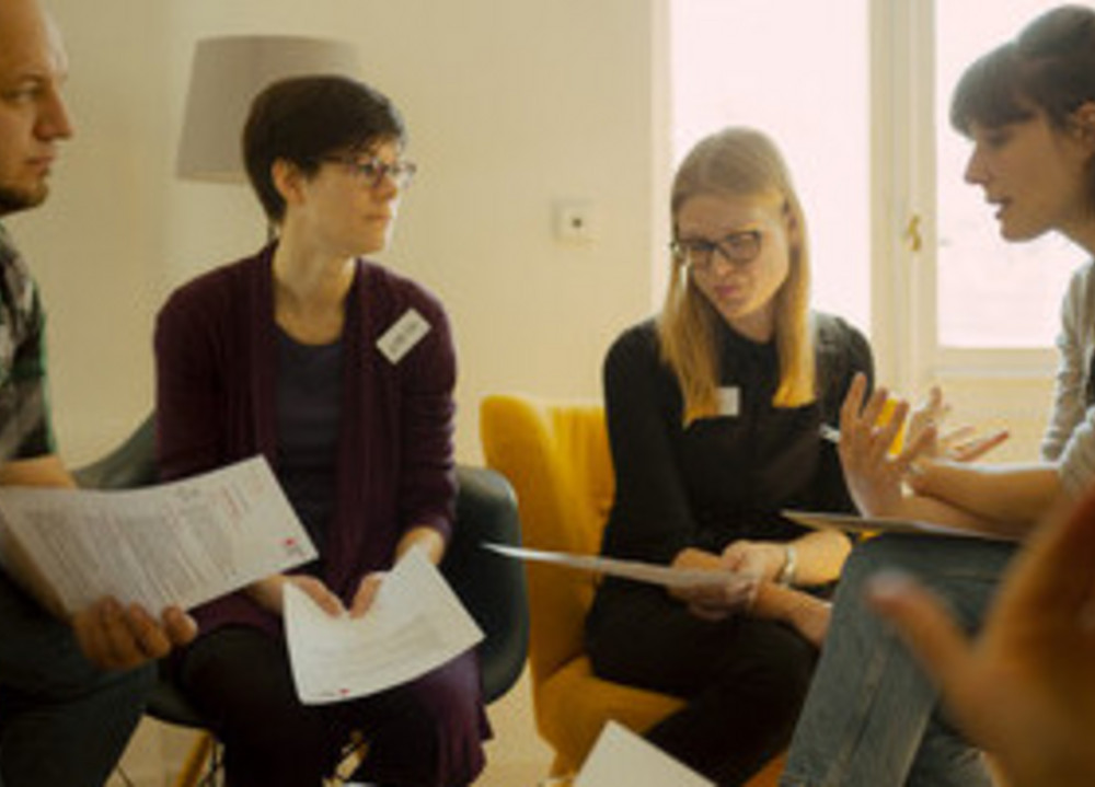 Mehrere Personen sitzen im Stuhlkreis und lesen einen Dialog.