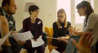 Mehrere Personen sitzen im Stuhlkreis und lesen einen Dialog.