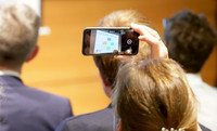 Eine Person fotogarfiert mit einem Smartphone während einer Konferenz