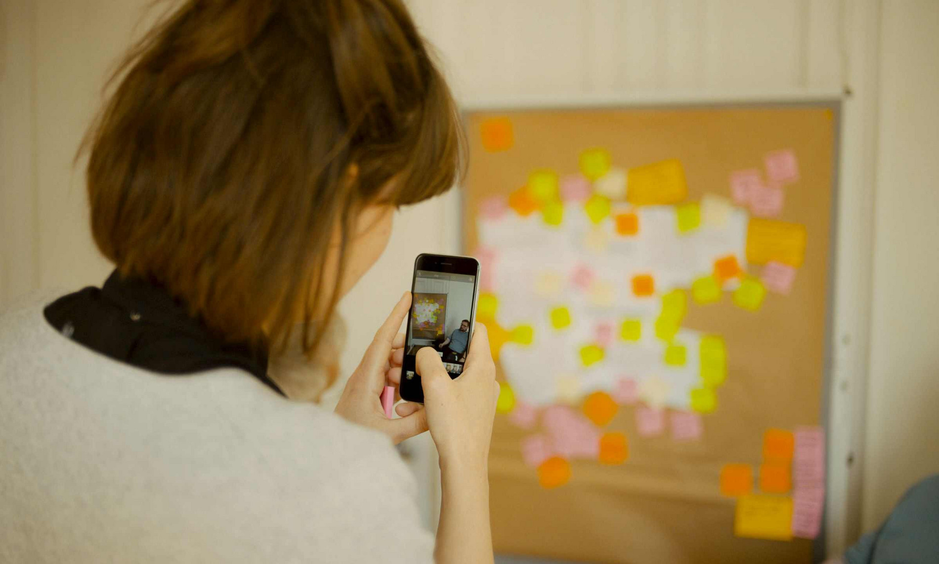 Eine Frau fotografiert mit ihrem Smartphone eine Wand mit bunten Klebezetteln
