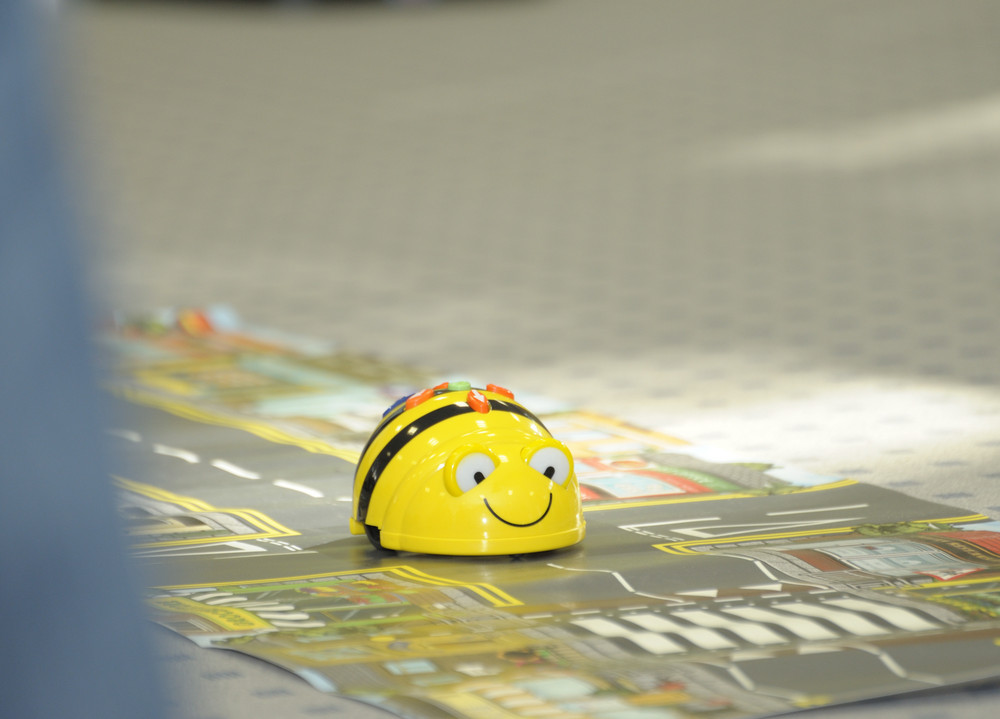 Ein Bee-Bot auf einem Spiel-Teppich mit Straßen und Gebäuden.