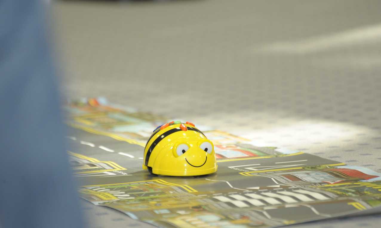 Ein Bee-Bot auf einem Spiel-Teppich mit Straßen und Gebäuden.