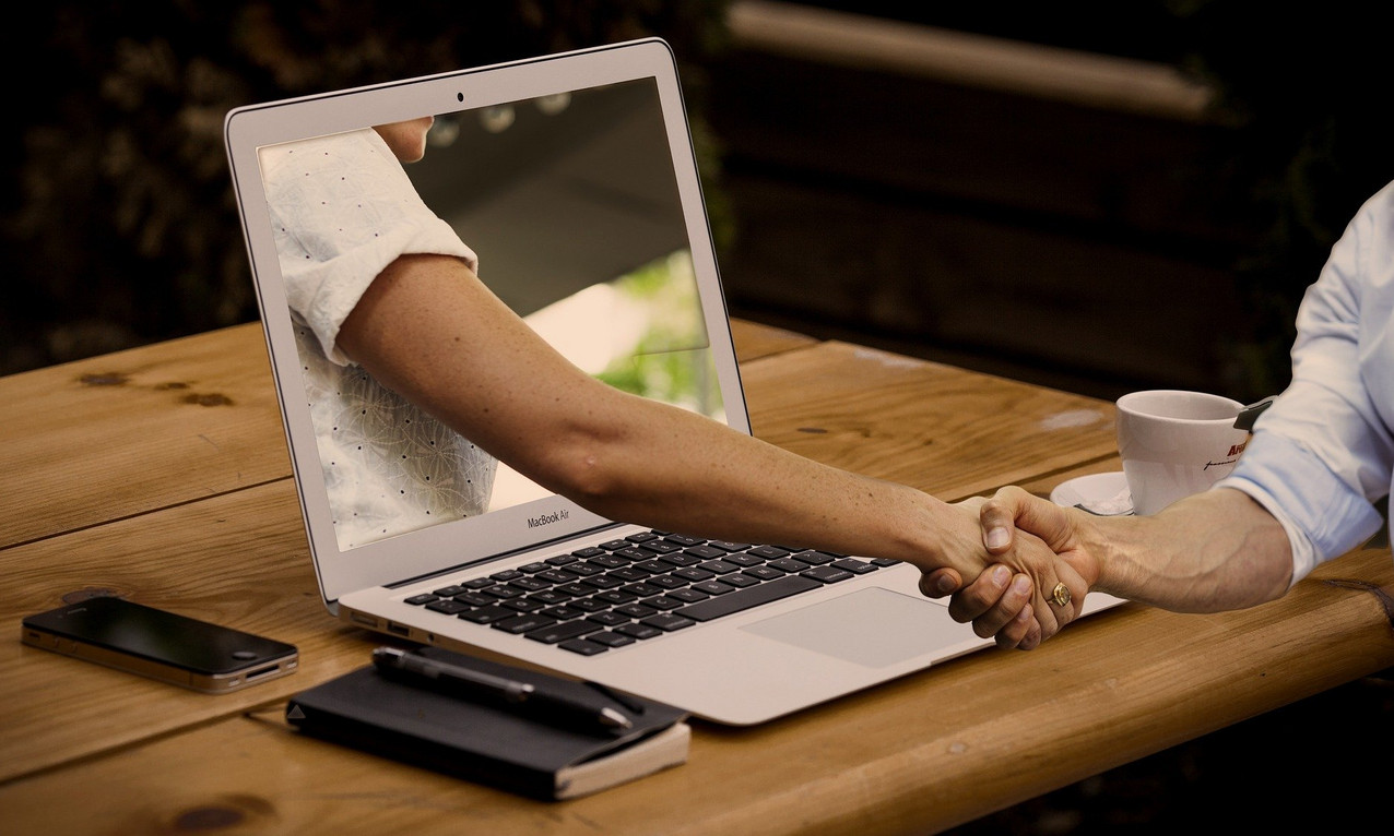 Eine Hand greift aus einem Laptop und schüttelt die Hand der Person vor dem Laptop.