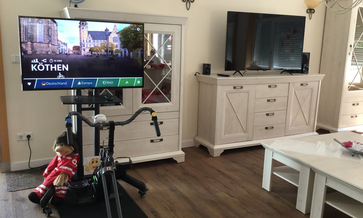Indoor-Fahrrad mit Flachbildschirm für eine virtuelle Fahrradtour durch Köthen und Mobiliar in einer Seniorenresidenz