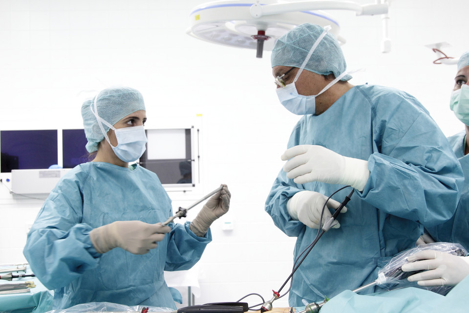 OP-Saal Zwei im Operationssaal stehende Personen in OP-Kleidung und Handschuhen, eine hält ein chirurgisches Instrument