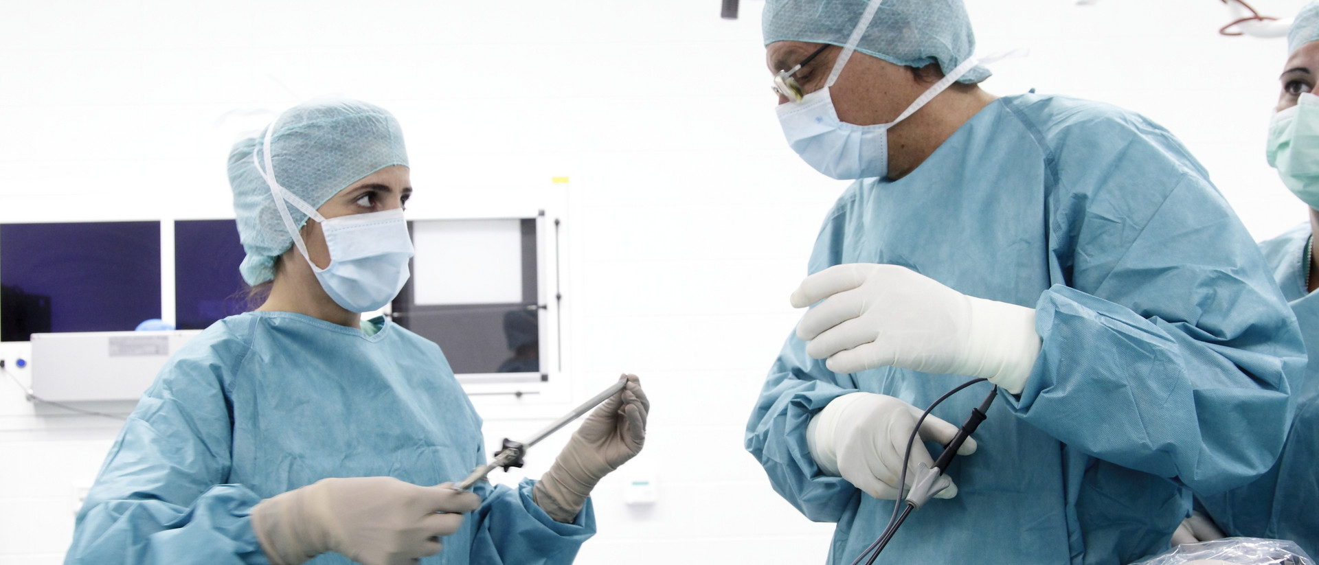 Zwei im Operationssaal stehende Personen in OP-Kleidung und Handschuhen, eine hält ein chirurgisches Instrument