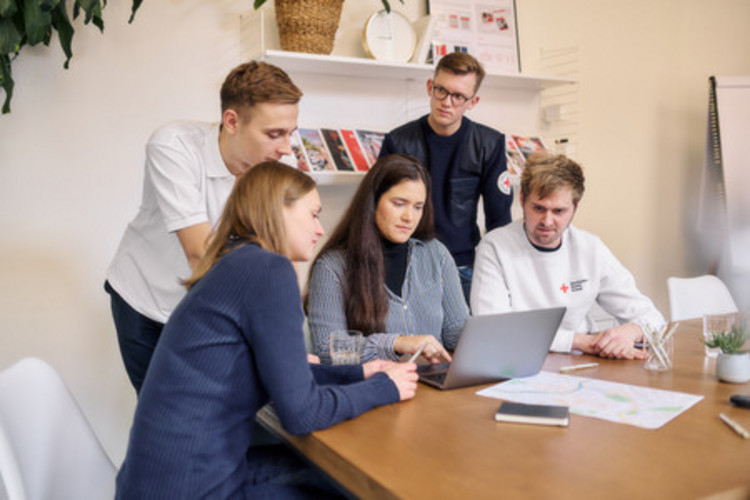 Fünf Personen am Schreibtisch schauen auf einen Laptop