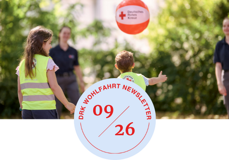 Kinder mit Warnwesten spielen mit einem Ball, auf dem das Logo des Deutschen Roten Kreuzes zu sehen ist, im Hintergrund stehen zwei Erwachsene in dunkler Kleidung