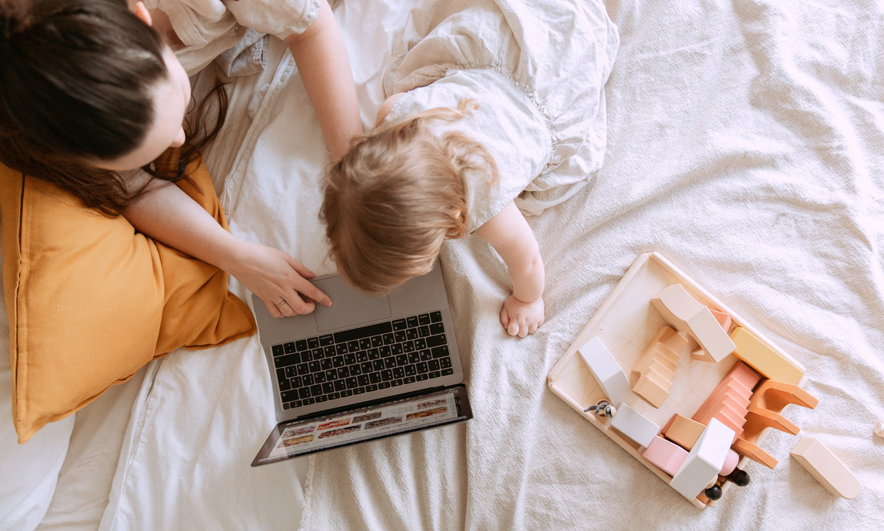 Mutter und Kleinkind auf einem Bett vor. Sie sehen auf einen Laptop. Fotos aus Vogelperspektive