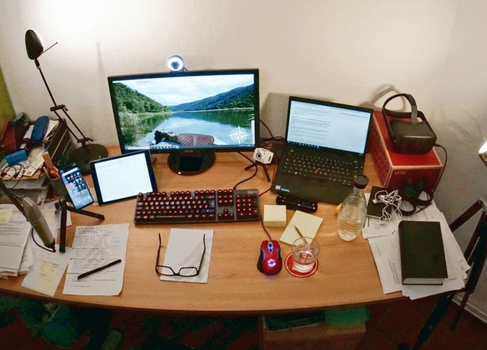 Ein Büroschreibtisch voller Büromaterialien, Unterlagen, einem Laptop und einem Monitor