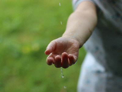 eine Kinderhand fängt Regen auf im Hintergrund grünes Gras