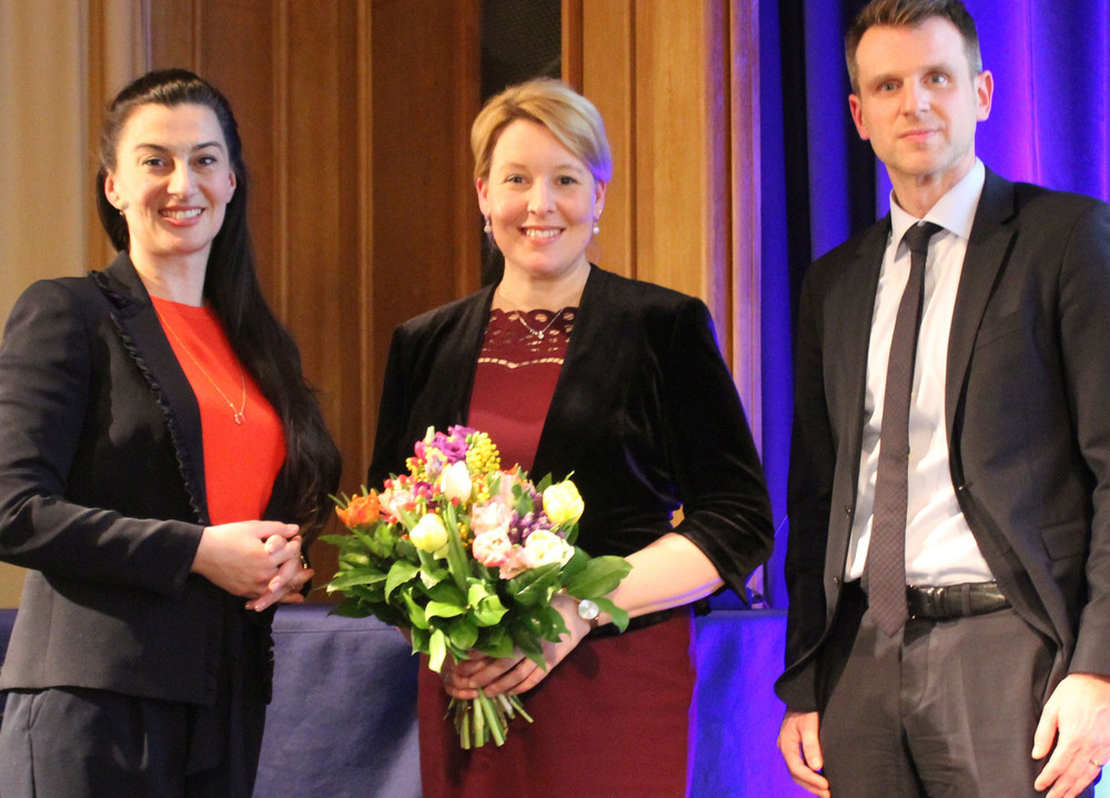 Franziska Giffey mit Blumen und zwei weitere Personen stehend auf einem Podium