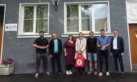 Gruppe aus sieben Personen steht vor einem Gebäude mit Rotem Kreuz