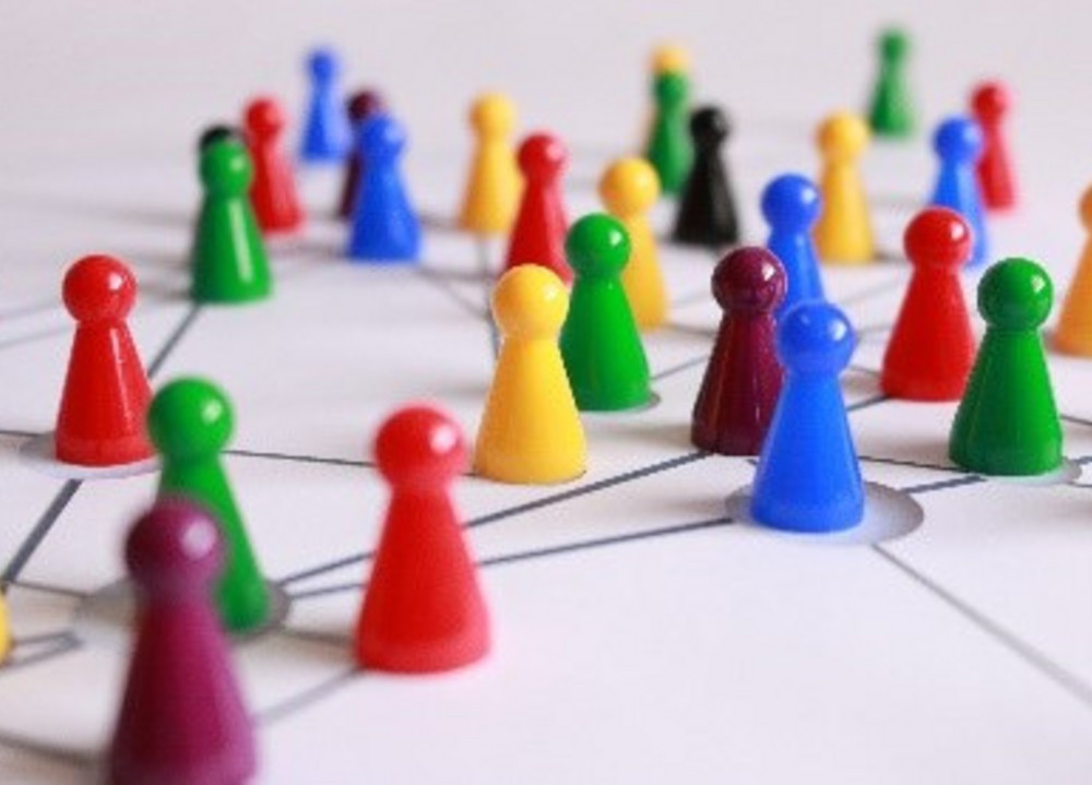 Viele Mensch-Ärger-Dich-Nicht-Spielfiguren in rot, blau, gelb und grün. Sie sind durch Lininen miteinander verbunden.