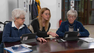 Seniorinnen sitzen mit einer Studentin vor Tablets