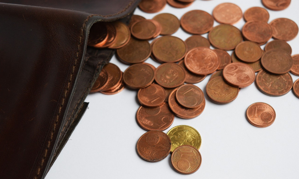 Quelle: Pixabay Das Bild zeigt eine Brieftasche auf einem Tisch und davor verstreut liegendes Kleingeld.