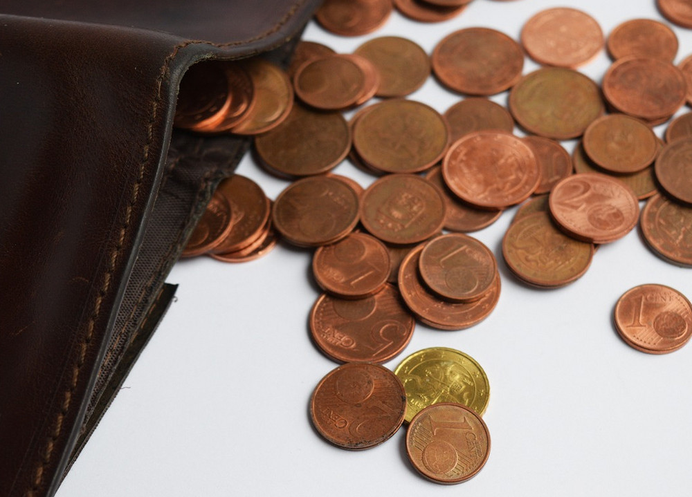 Das Bild zeigt eine Brieftasche auf einem Tisch und davor verstreut liegendes Kleingeld.