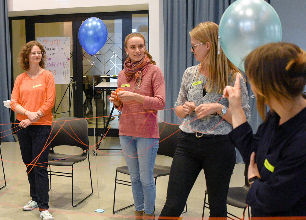 Mehrere Leute stehen im Kreis und machen ein Warmup-Spiel mit Luftballons und einem Seil