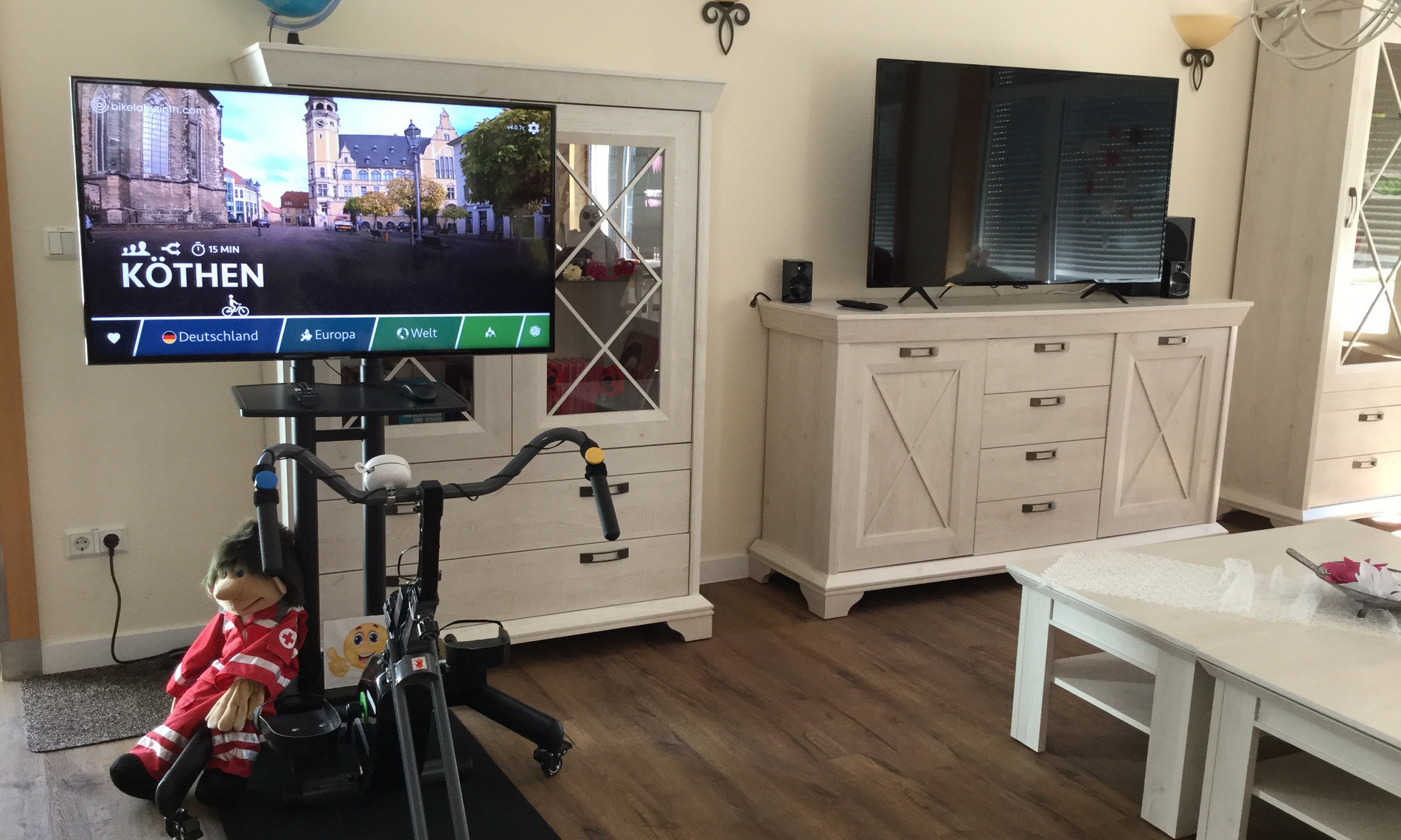 Links ein Flachbildschirm verbunden mit einem Heimtrainer; Foto aus dem Wohnzimmer. 