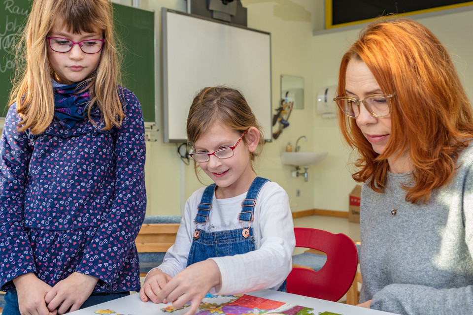 Schulassistenz, Schulkind und Begleitperson in der Schule beim Puzzlen.