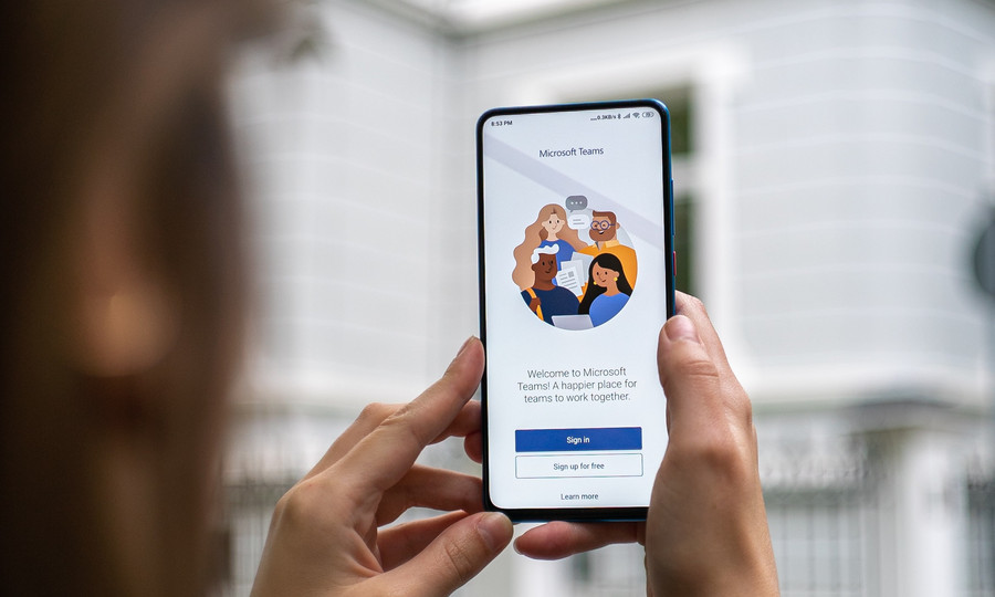 Smartphone liegt in der Hand. Auf dem Bildschirm des Handys ist ein Abbild der Applikation Microsoft-Teams zu sehen.