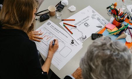 Person an einem Tisch füllt ein Formular beim Design-Think-Prozess aus. Auf dem Tisch liegen viele Büromaterialien wie Post-Its und Stifte.