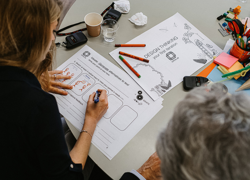 Person an einem Tisch füllt ein Formular beim Design-Think-Prozess aus. Auf dem Tisch liegen viele Büromaterialien wie Post-Its und Stifte.