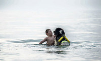 Kind und Hund mit gelbem Schwimmgeschirr im Wasser, beide blicken sich an.