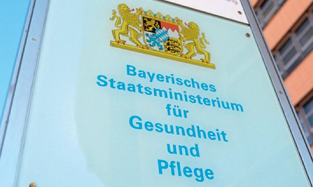 Ein Foto vom Eingangsschild auf dem steht "Bayerisches Staatsministerium für Gesundheit und Pflege", darüber das Wappen Bayerns