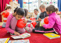 Kinder spielen in einer Kita auf einem Teppich mit Ballons und lesen Bücher