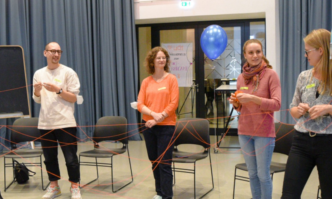Vier Mitglieder der Social Innovation Community bei der Durchführung einer kreativen Workshop-Methode mit einem Bindfaden und Luftballons.