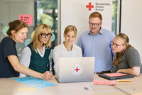 Fünf Personen sitzen an einem Tisch und schauen auf einen Laptop mit Deutschem Roten Kreuz-Logo.