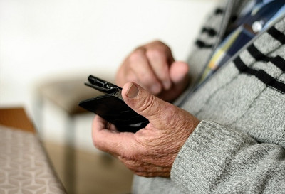 Das Bild zeigt die Hände einer älteren Person, die ein Smartphone halten.