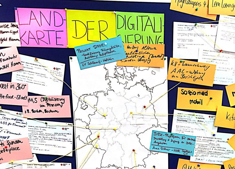Eine Wand voller Post-Its, in der Mitte hängt eine Deutschlandkarte mit Linien und über ihr steht "Landkarte der Digitalisierung".