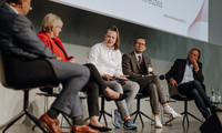 Auf dem Bild sitzen 5 Personen in einer Reihe auf einem Podium und diskutieren.