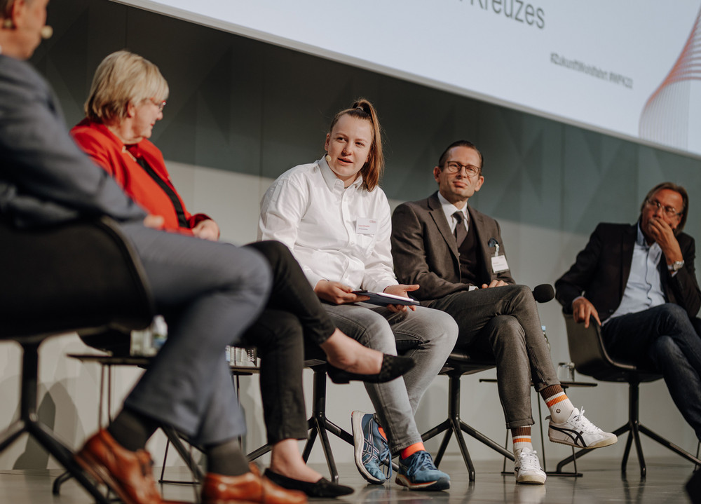 Auf dem Bild sitzen 5 Personen in einer Reihe auf einem Podium und diskutieren.