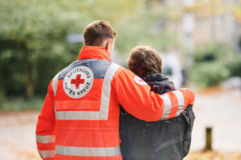 Symbolfoto, Helfer vom DRK legt seinen Arm um eine Person