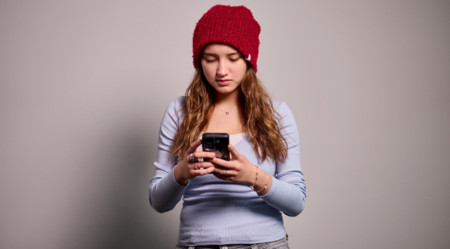 mit roter Strickmütze und hellblauem Langarmshirt blickt auf ihr Smartphone