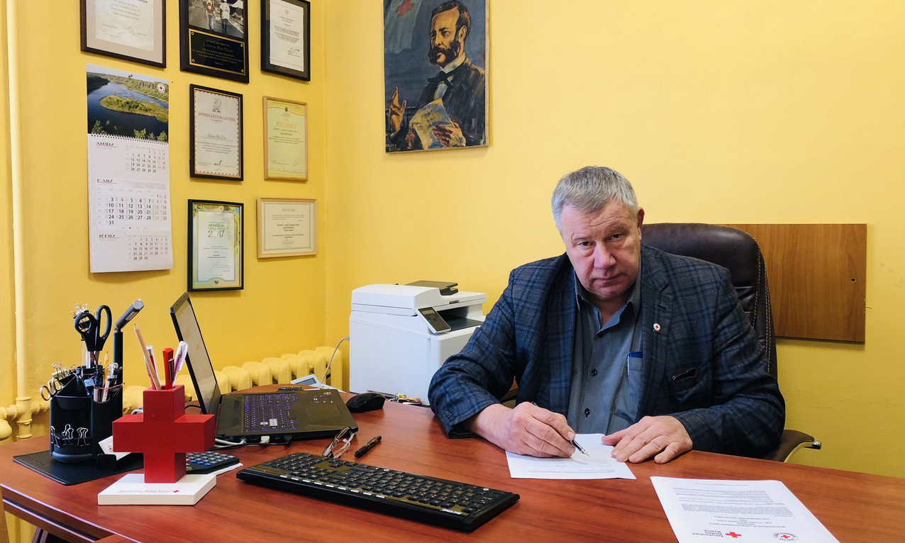 Uldis Likops, Generalsekretär des Lettischen Roten Kreuzes unterschreibt ein Dokument. Im Hintergrund ein Foto von Henry Dunant