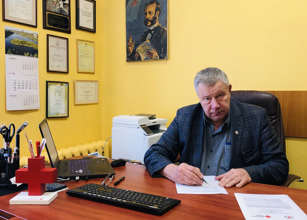 Uldis Likops, Secretary General of the Latvian Red Cross. Sitting at a desk. Signing a document.