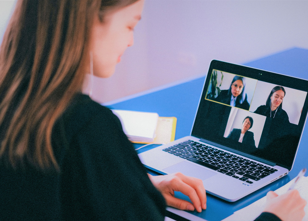 Eine Frau sitzt vor einem Laptop auf dem eine Videokonferenz läuft.