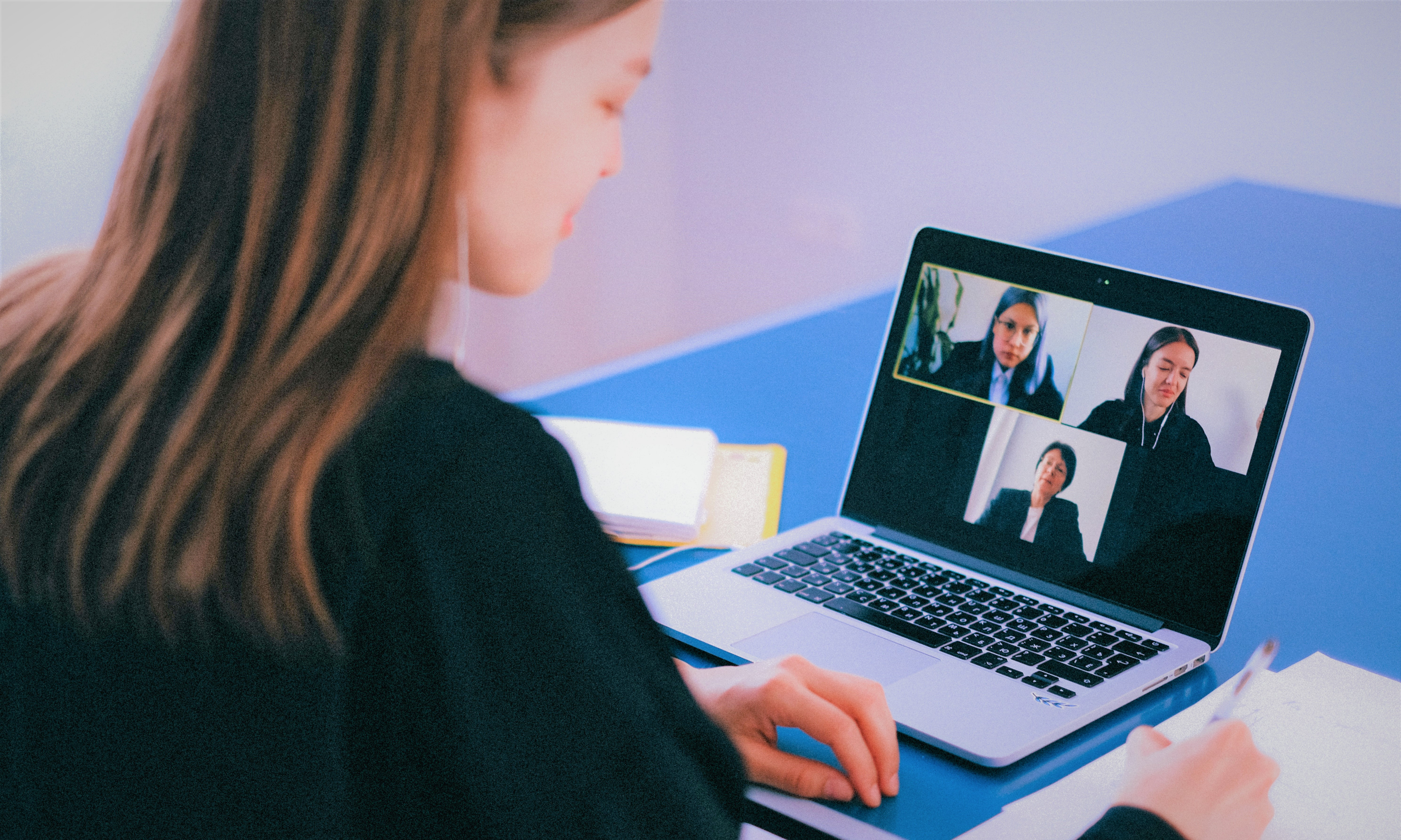 Eine Frau sitzt vor einem Laptop auf dem eine Videokonferenz läuft.
