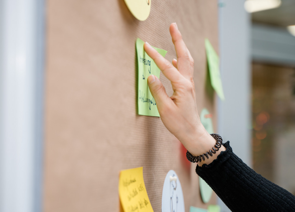 Hand einer Frau, die ein Post-it an eine Papierwand klebt