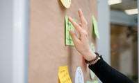 Hand einer Frau, die ein Post-it an eine Papierwand klebt