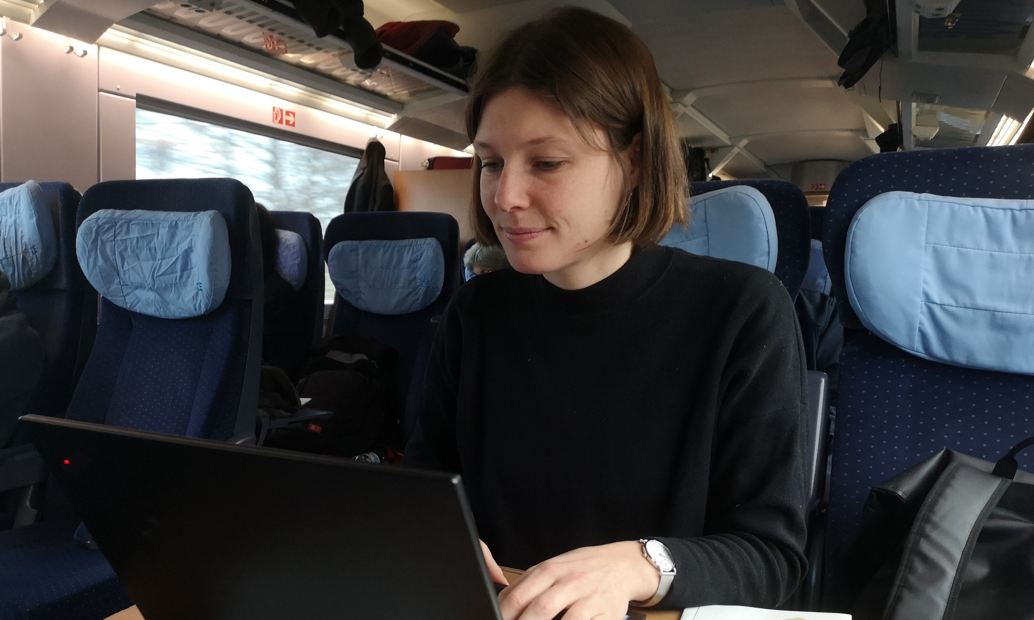 Susanne sitzt im Zug und arbeitet an ihrem Laptop.